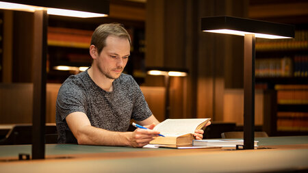 一名男子坐在阅览室的桌子旁，看着一本书。