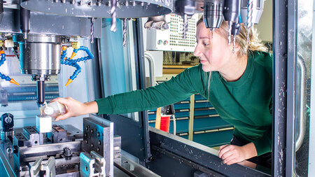 Eine junge Frau arbeitet a einer Werkzeugmaschine女士。