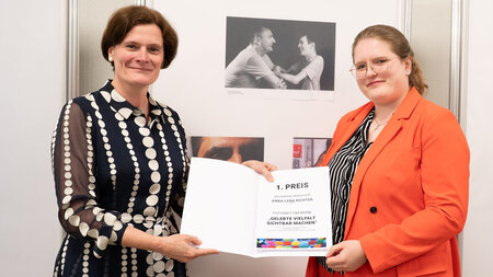 Zwei Frauen halten vor einer Ausstellungstafel eine Urkunde in den Händen.