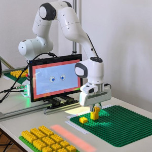 Robot-arm setup including display with eyes constructing something with lego duplo like bricks.