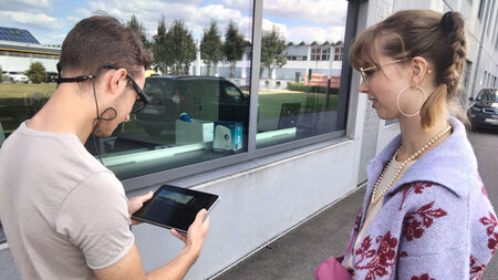 Ein junger Mann und eine junge Frau stehen nebeneinander und blicken auf ein Tablet.