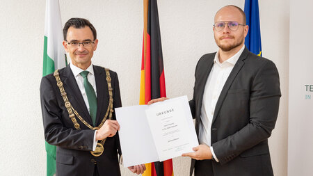 Zwei Männer im Anzug halten eine Urkunde fest.