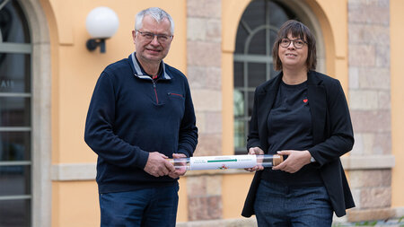 Ein Mann und eine Frau halten einen Staffelstab aus Glas fest