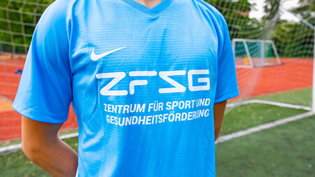 Eine Person, die auf einem Sportplatz steht, trägt ein bedrucktes Sport-Shirt.