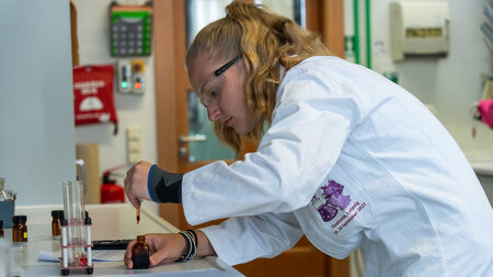 Eine Schlerin im weien Kittel experiementiert im Chemielabor.