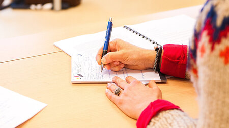 Eine Hand liegt auf einem Tisch auf und hält einen Stift. 