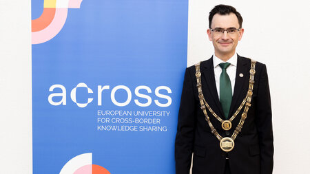 A man in a suit and wearing an Amstkette stands next to a banner.