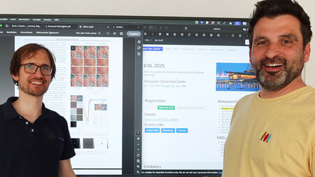 Zwei Männer stehen vor einem großen Bildschirm.