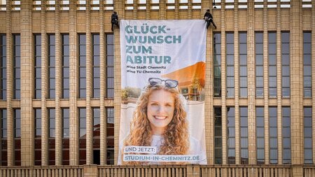 Ein riesiger Banner hängt an einer Gebäudefassade.