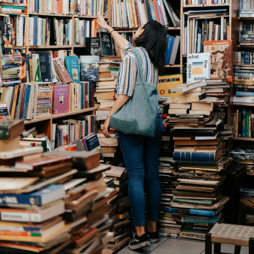 Eine Frau vor einem Bücherregal, auch im Vordergrund sind viele Bücher zu sehen.